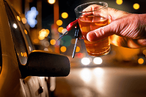Man holding a glass of alcohol getting into a car