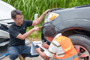 Two accident reconstruction experts analyzing damage on a vehicle. 