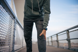 young man walking on a bridge grabbing knee in pain